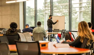 Instructor writing on a whiteboard while students listen in a classroom.