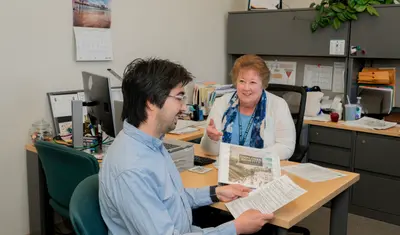 A new CSUMB employee sits across a desk from a HR professional holding a binder of benefits information.