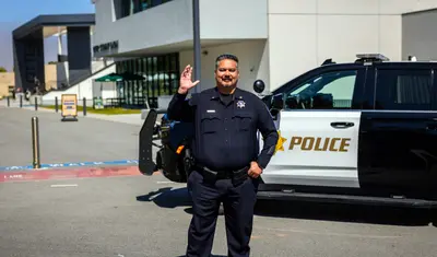A portrait of a UPD officer smiling and waving in front of a squad car by the OSU