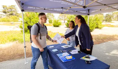 Two people manning a table giving out a social work flyer to a student visiting the stand