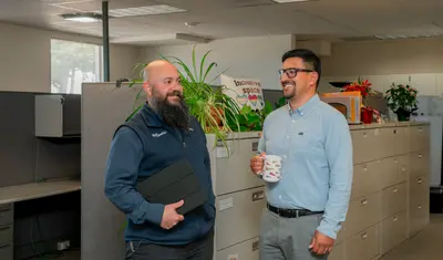 Two human resources professionals stand facing one another and chatting in an office.