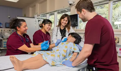Nursing student and teacher around a hospital bed with mannequin