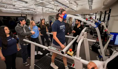 A professor giving a presentation to a group of students while a student is on the treadmill