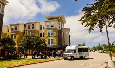 “The Wave” campus shuttle parked in front of university buildings.