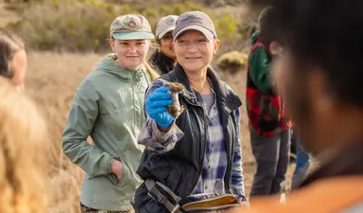 A CSUMB faculty member holds up a small mammal during an outdoor wildlife field activity.