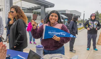 Student holding a CSUMB pennant and smiling at the camera.