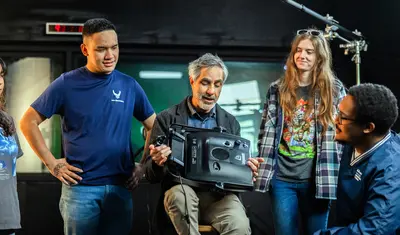 Professor holding LED light panel with students looking at him talk