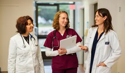 A nursing student in a scrub and two professors standing in a walkway talking together