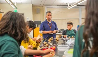 An instructor guiding a small group of students as they work on hands-on project.