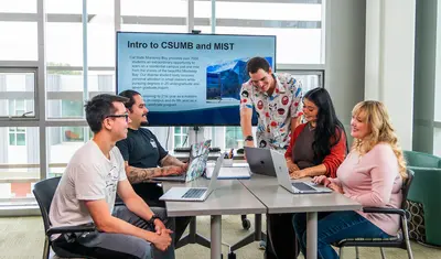 CSUMB instructional science and technology faculty guide students during a collaborative class session, reviewing course materials on laptops and a shared screen.