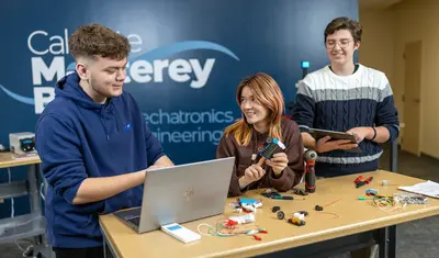 A group of three mechatronics students behind a mechatronics display table