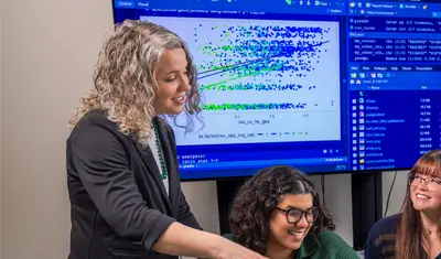A faculty member guides students through data analysis, fostering collaboration and hands-on learning with technology.