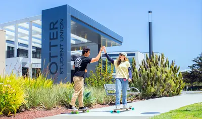 Two people hi fiving in front of the otter student union