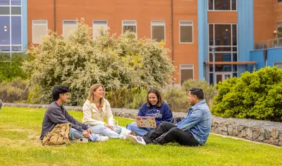 Group of students sitting on the grass in front of the Chapman Science Building.