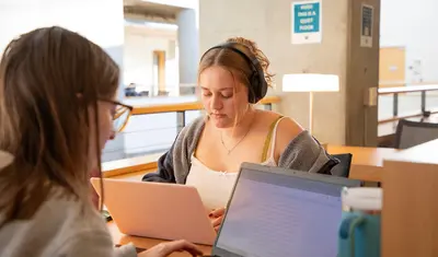 Students focus on individual study in a quiet campus space, using laptops to support their academic work.