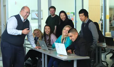 A faculty member engages students in a collaborative classroom setting as they work together on laptops and share ideas.