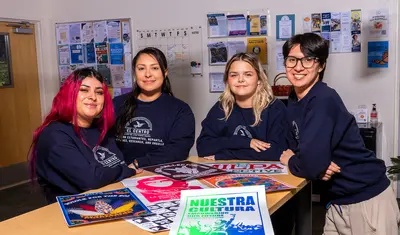 Students at a table of El Centro event posters.