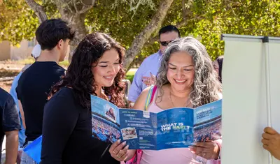 Student and parent smiling while looking at a CSUMB brochure.