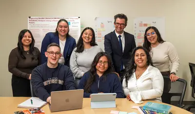 A combination of students and professors smiling for a photo together, with three people sitting at a table and five people standing behind them