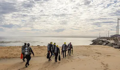 Group of scuba divers walking across the beach towards the ocean