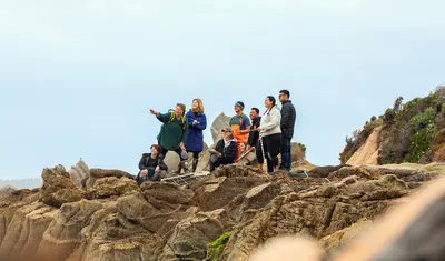 Marine science students gather on a rocky coastal outcrop during a field study, observing the shoreline and engaging in hands-on research within the natural environment near Monterey Bay at Cal State Monterey Bay.