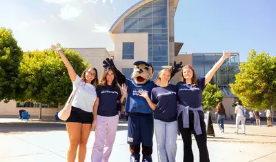 Students and the campus mascot pose outside a central building, celebrating school spirit and a welcoming community.