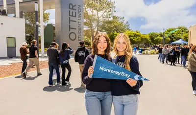 Students hold a Monterey Bay sign on campus, highlighting school spirit and community engagement.
