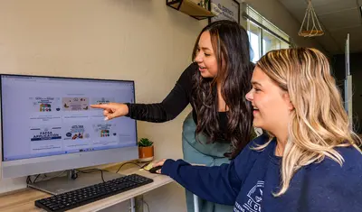 A staff member guides a student through online resources, highlighting personalized support and academic success.