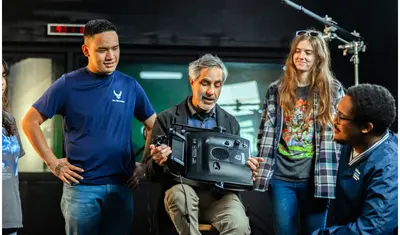 Professor holding LED light panel with students looking at him talk