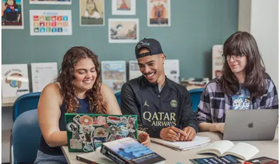 A group of three students sitting and smiling at a computer together.
