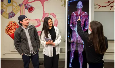 A student is giving a presentation using a digital anatomy board to two other students