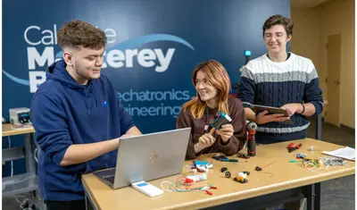A group of three mechatronics students behind a mechatronics display table