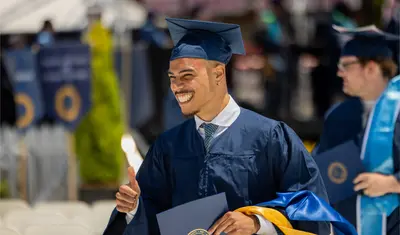 A student in cap and gown holding a diploma in his hand