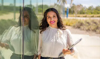 A masters of business administration professor smiling at the camera while leaning against a glass wall