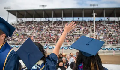 An alumni in cap and gown waves at the crowd
