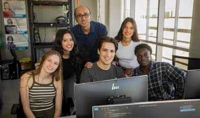 A group of students and a professor in front of a computer in the business and information technology building