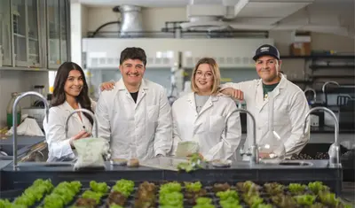 Four students standing next to each other in a lab and smiling for the photo