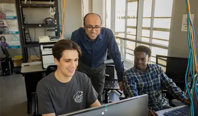Two students working while their professor oversees them in the business and information technology building