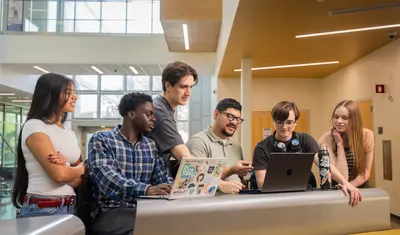 Group of students collaborating on a computer in the Business and Information Science building.