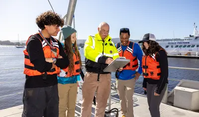 A group of four students and a professor on a dock collaborating