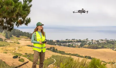 An environmental science student holding a remote controller and is flying a drone overhead