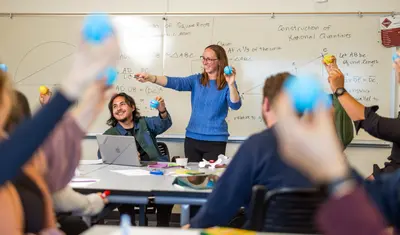Professor and students all holding up a blue ball while she is smiling at them