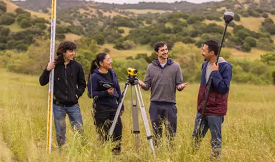 A group of four AES students holding surveying tools while collaborating together
