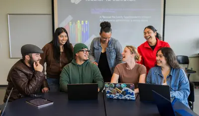 Group of students smiling and talking together in a classroom.