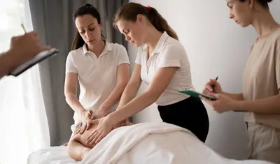 Students receive instruction while practicing massage techniques on a client in a classroom.