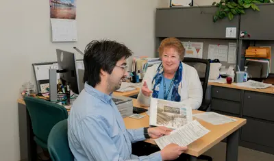 A new CSUMB employee sits across a desk from a HR professional holding a binder of benefits information.