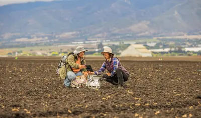 Two people leaning down together in a field talking.