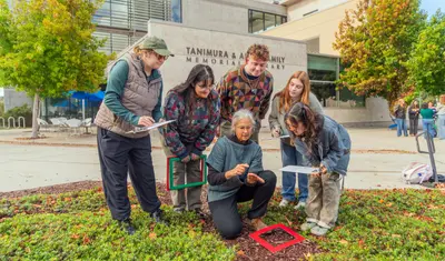 A CSUMB environmental studies instructor and students conduct a hands-on biodiversity survey outside the library, using quadrats and clipboards to collect field data.