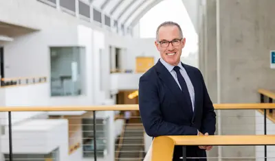 CSUMB Provost Andrew Lawson stands by a railing inside a modern campus building.