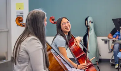 A ���ӽ紫ý cello student laughs warmly during a lesson, sharing a lighthearted moment with her instructor while holding her instrument.